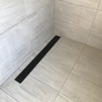 Black strip shower drain in porcelain tiled open shower